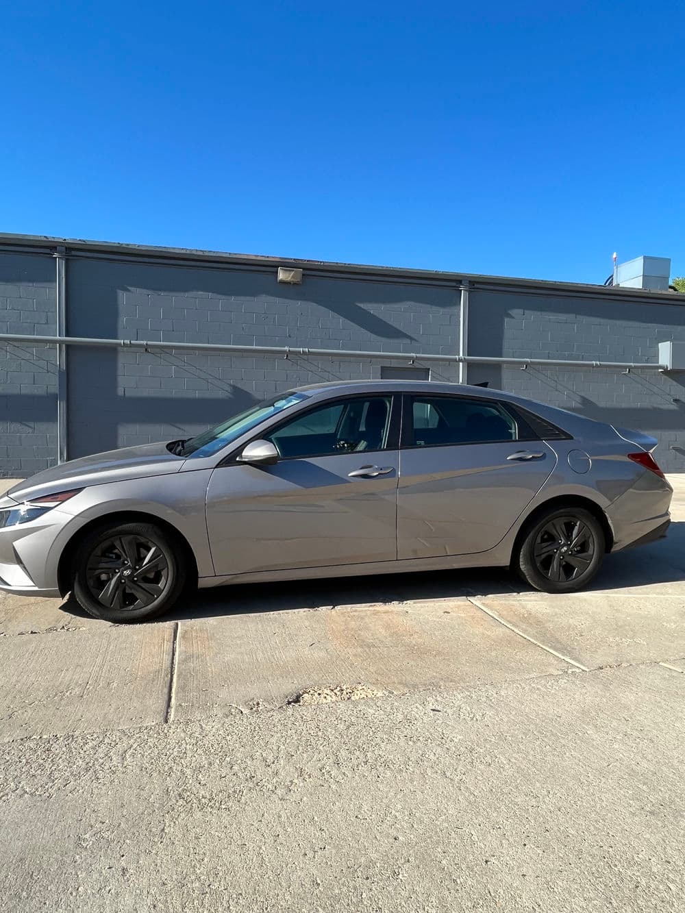 Silver sedan parked beside a gray building under clear blue sky.