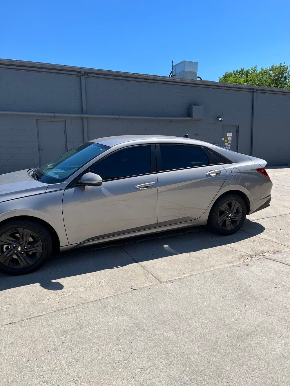Silver sedan with tinted windows parked beside a gray building on a sunny day.