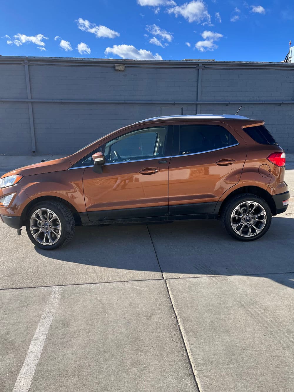 Side view of a bronze SUV parked on a driveway with a blue sky background.